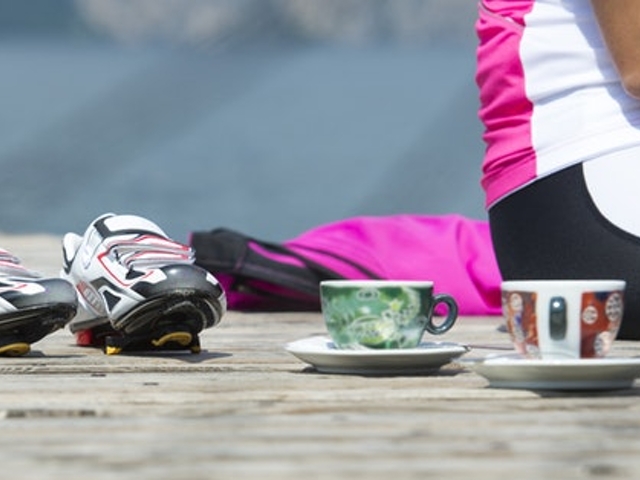 Eine sitzende Frau mit Sportsachen, zwei Kaffeetassen und Sportschuhen