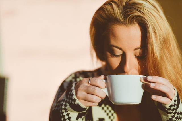 Eine blonde Frau trinkt genüsslich ihren Kaffee aus einer Kaffeetasse.