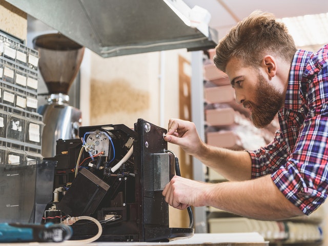 Ein junger Mann repariert einen Kaffeevollautomaten