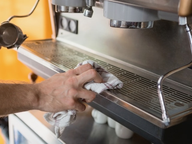 Ein Mann reinigt den Kaffeevollautomaten mit einem Küchentuch