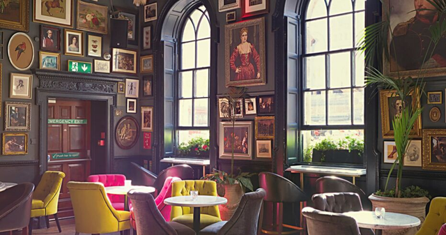 Ein Cafe eingerichtet mit Vintage-Sesseln in knalligen Farben und vielen altmodischen Bildern in goldenen Rahmen