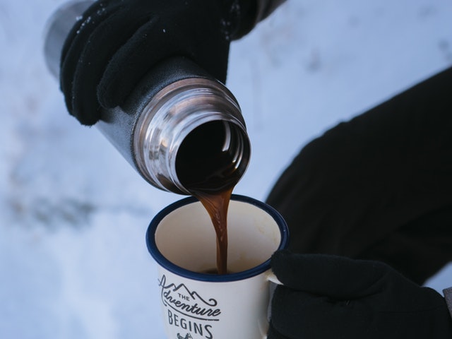 Kaffee wird aus der Thermoskanne in einen Kaffeebecher geschüttet